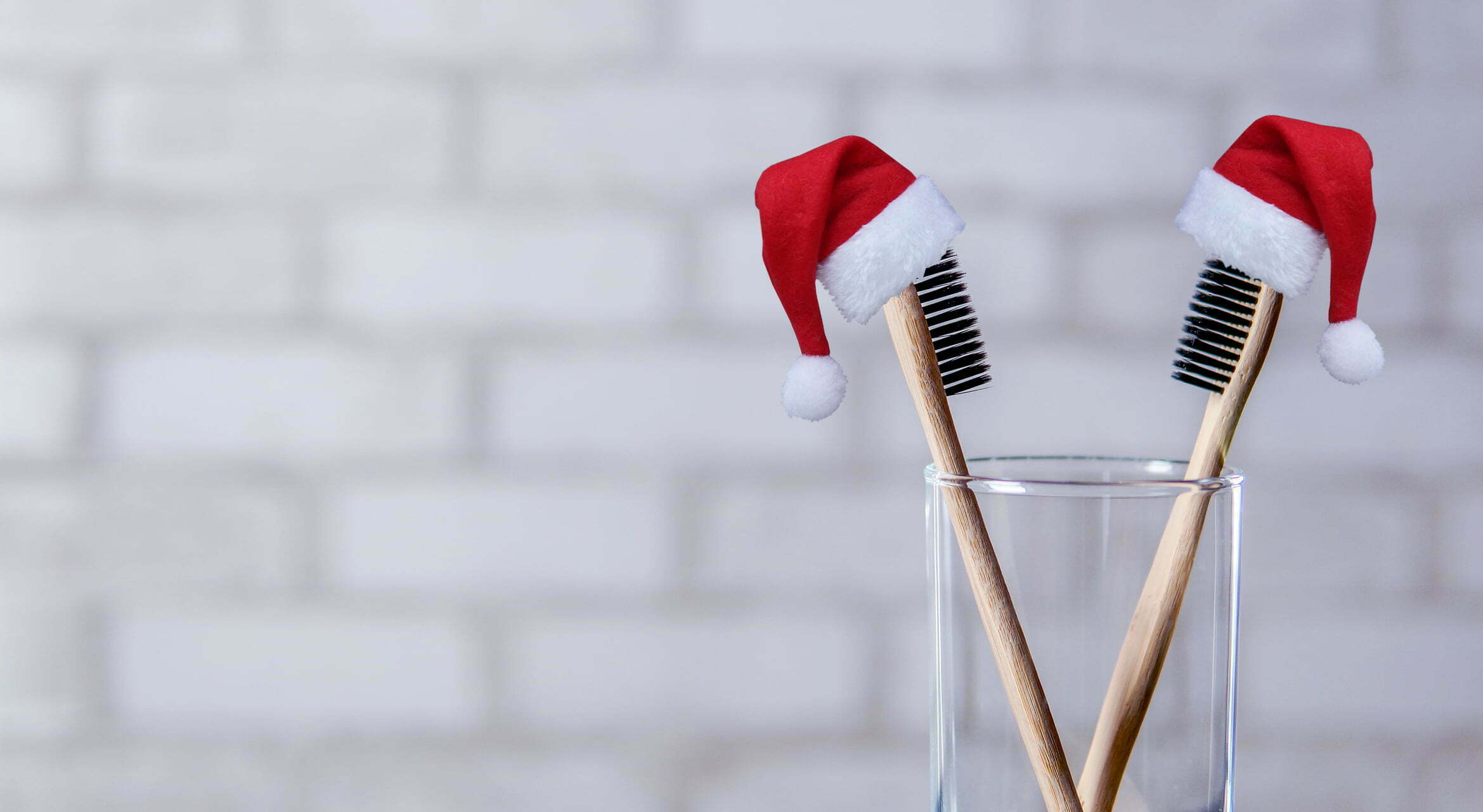 Two toothbrushes in the glass wearing santa hats