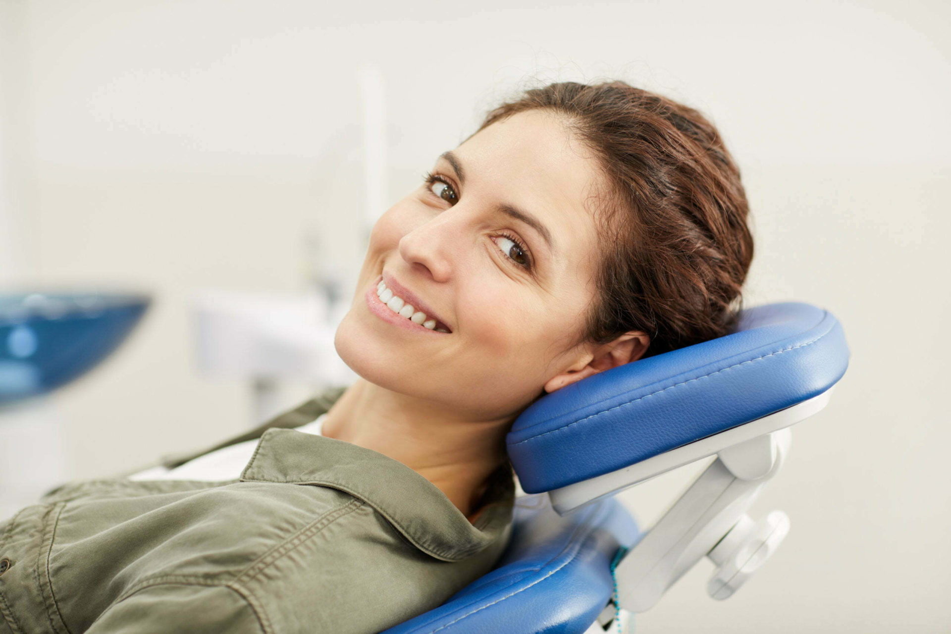 Portrait of smiling young woman lying in dental chair and looking at camera