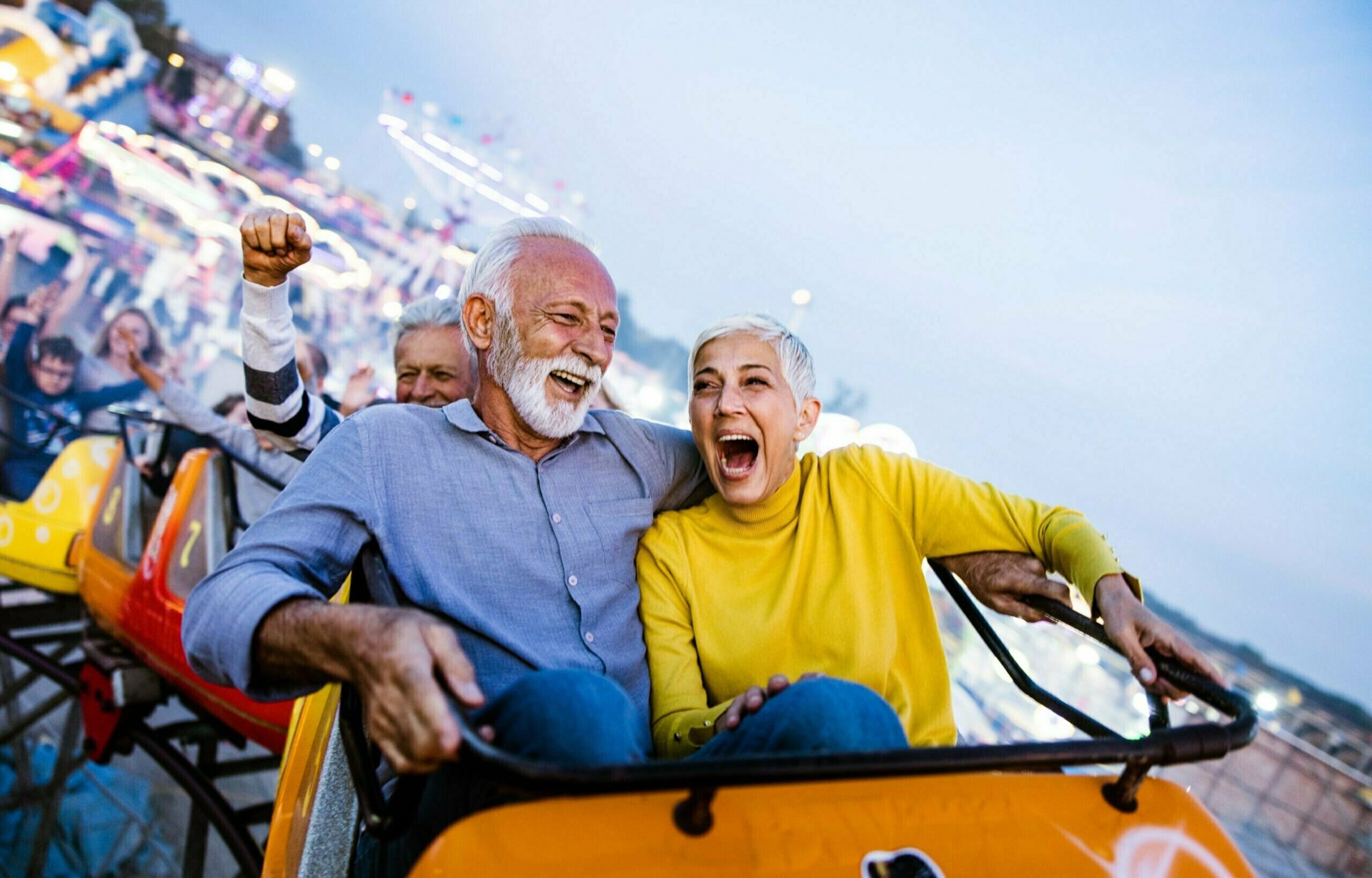Cheerful senior couple having fun while riding on rollercoaster at amusement park